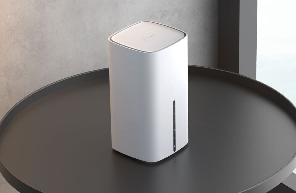 Router TP-LINK Archer NX210 5G Biały, prostokątny router o zaokrąglonych krawędziach stoi na okrągłym, czarnym stole przy ścianie o surowym, betonowym wykończeniu, opis