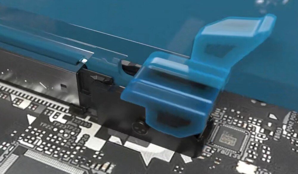 Płyta główna ASROCK B850 RIPTIDE WIFI Zbliżenie na plastikowy zatrzask gniazda karty graficznej wykonany z półprzezroczystego, niebieskiego materiału. Mechanizm jest zamontowany na czarnym laminacie obok srebrnych elementów gniazda