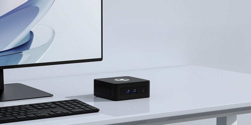 Komputer QOOBE II AP1215U Czarny miniaturowy komputer z portami USB ustawiony obok monitora i klawiatury na białym biurku, opis