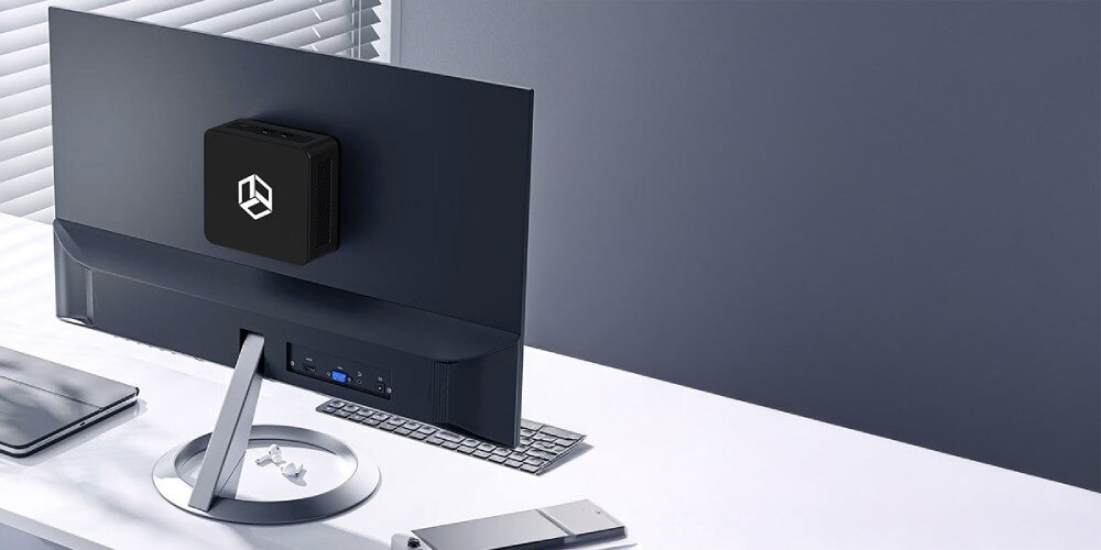 Komputer QOOBE II AP1215U Mały komputer przymocowany z tyłu monitora na uchwycie, ustawiony na jasnym biurku z klawiaturą i myszką, zintegrowana karta graficzna, obraz, wyjścia HDMI