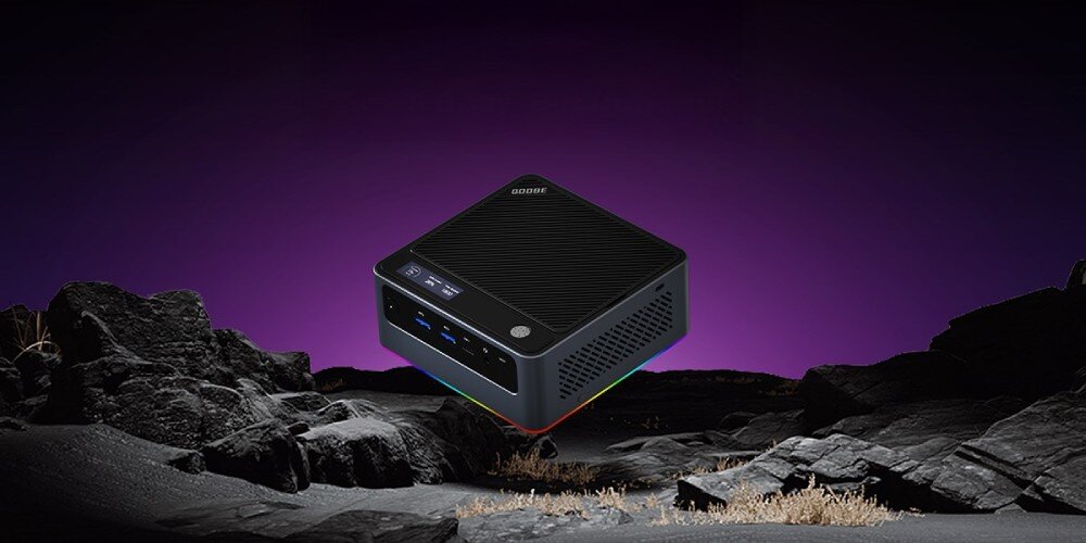 Komputer QOOBE U155H Mały komputer z logo na obudowie pokazany w scenerii skalistego krajobrazu z fioletowym niebem, łączność, Wi-Fi, Bluetooth, porty