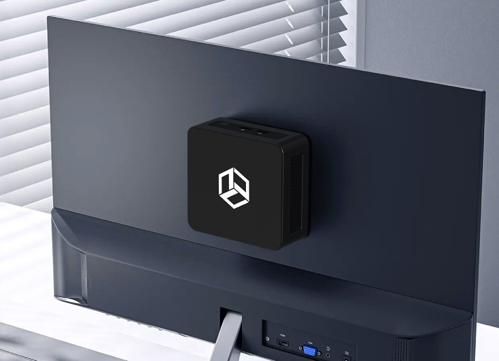 Komputer QOOBE II AP-1340 Urządzenie zamontowane z tyłu monitora w jasnym pomieszczeniu z żaluzjami, logo jest widoczne na tylnej ściance urządzenia, energooszczędność, środowisko, pobór prądu