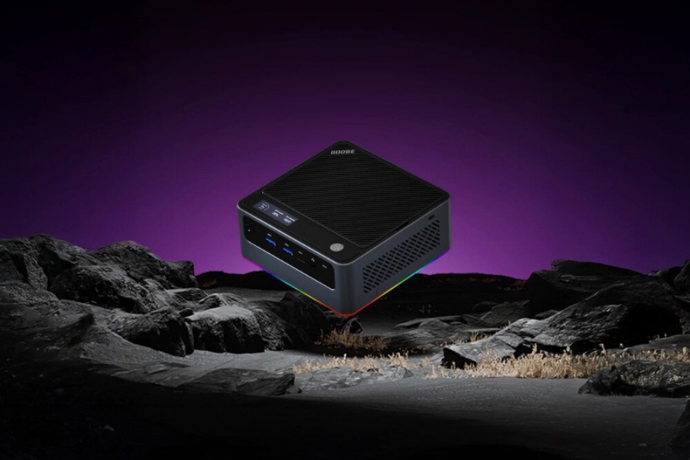 Komputer QOOBE U155H Widok na mini pc lewitujący nad ciemnym, skalistym podłożem na fioletowym tle, urządzenie posiada czarną obudowę z widocznym wyświetlaczem i podświetleniem, pamięć RAM, rozbudowa