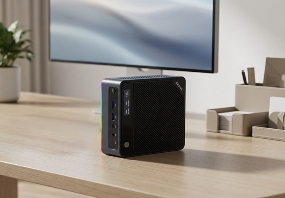 Komputer QOOBE U155H Komputer mini pc ustawiony pionowo na biurku przed monitorem, widoczna struktura obudowy z wyświetlaczem na górnej części i wielokolorowym podświetleniem, łączność bezprzewodowa, złącza
