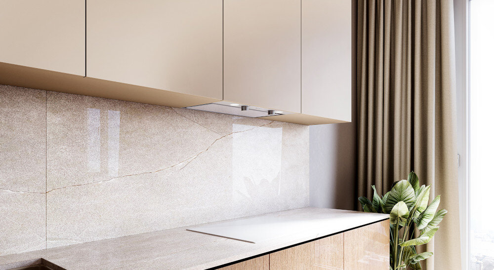 OKAP GLOBALO FLUXIME Zdjęcie przedstawia fragment kuchni z jasnymi, gładkimi szafkami wiszącymi oraz blatami w beżowym odcieniu. Na środku ujęcia znajduje się elegancki okap podszafkowy z wbudowanym oświetleniem, a po prawej widoczna jest roślina doniczkowa stojąca przy dużym oknie szkło hartowane wyjątkowy design biała stal trwałość elegancka kuchnia