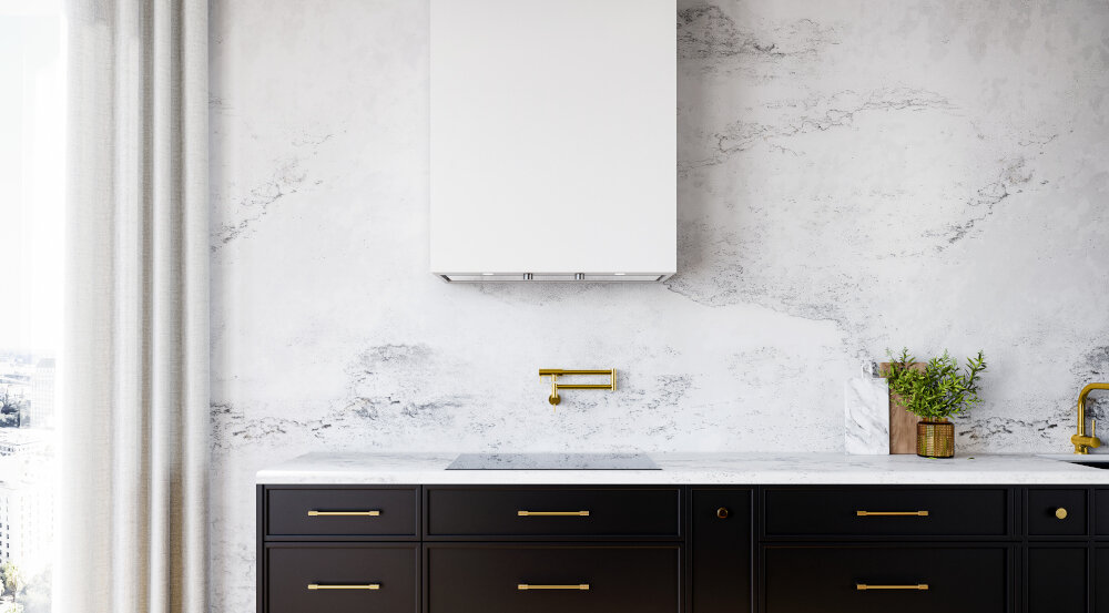 OKAP GLOBALO FLUXIME Obraz ukazuje centralną część kuchni z białym okapem zawieszonym nad płytą grzewczą i czarną zabudową z złotymi uchwytami. Marmurowa ściana tworzy eleganckie tło dla urządzenia szkło hartowane wyjątkowy design biała stal trwałość elegancka kuchnia