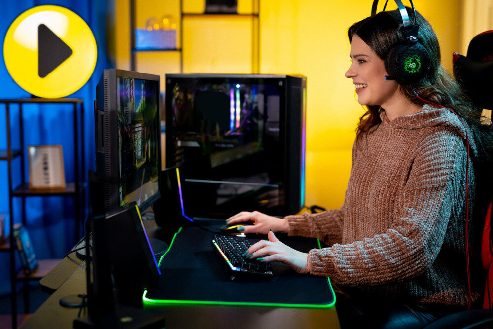 Komputer MAD DOG GeForce RTX4060 CS2 Reflex Edition BQ500FX-I11DR32 widok od boku, kobieta w słuchawkach gamingowych siedząca przy biurku grająca w grę, w tle komputer wygląd opis