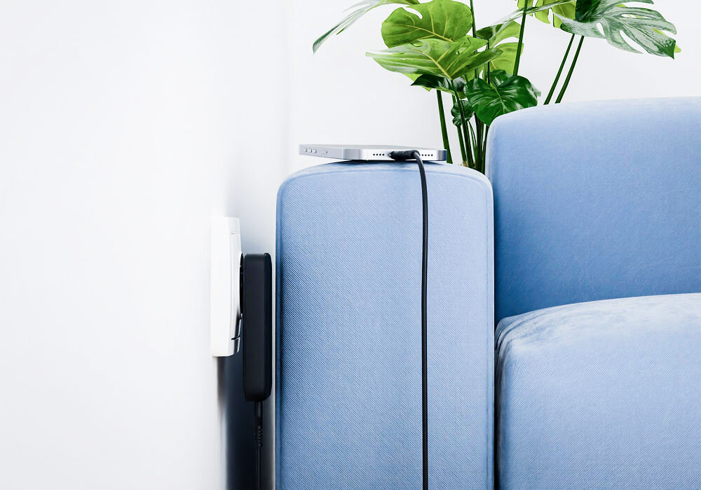 Ładowarka sieciowa USB-A - USB-C Qualo Ultimate QLS-GN-US-AC-45-01 GaN Ultra Slim PD 45W Czarny prezentacja ładowarki podłączonej do prądu wraz z telefonem w ciasnym i wąskim miejscu pomiędzy kanapą a ścianą