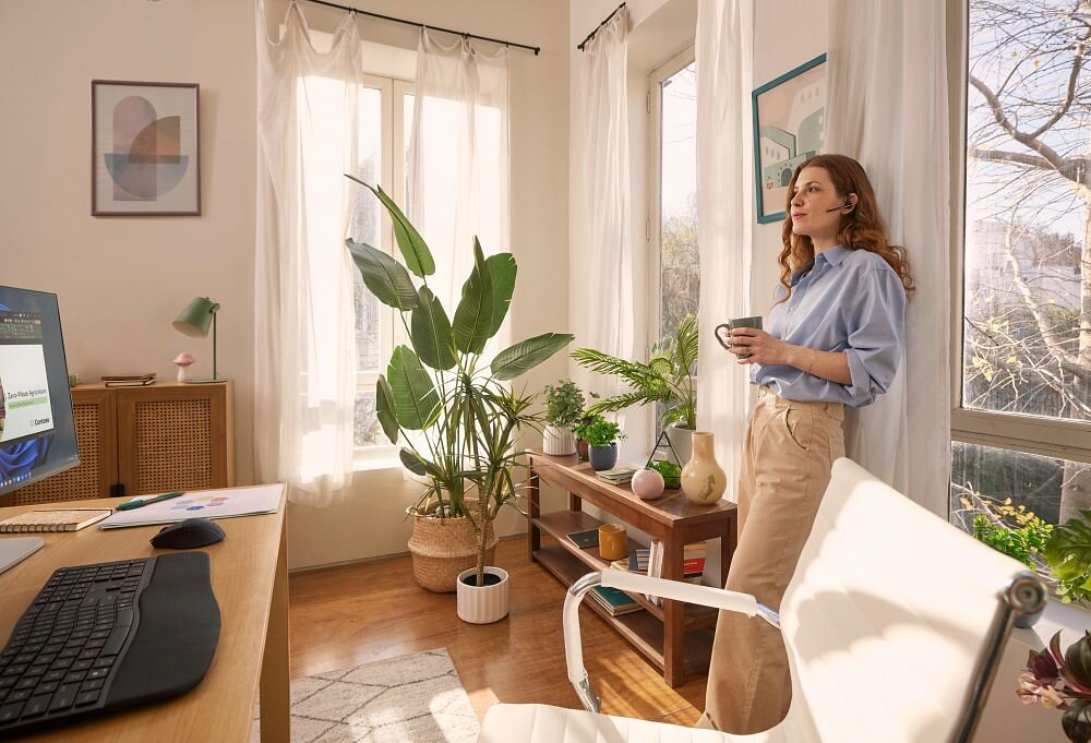 Słuchawka HP Poly Voyager Legend 50 VOY502 WindSmart filtracja wiatru, osoba z założoną słuchawką trzymająca kubek w ręku