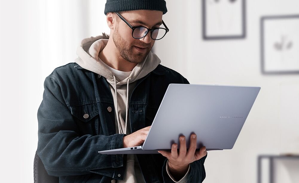 Laptop ASUS Vivobook S 16 OLED - Mężczyzna w okularach i kapeluszu korzysta z laptopa, skupiony na pracy lub nauce. Intel Core Ultra, AI, ASUS OLED 3K, klawiatura z podświetleniem RGB, ASUS AiSense