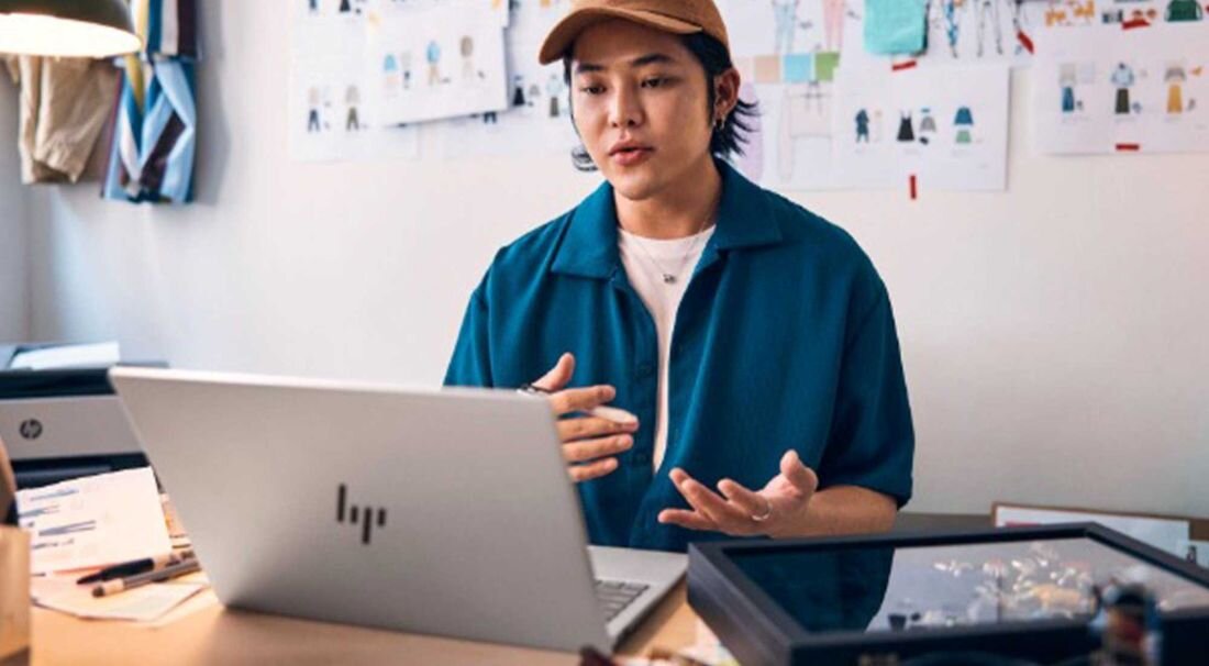 Mężczyzna siedzi przy biurku z laptopem HP Pavilion Plus 14. Karta Wi-Fi 6E Bluetooth 5.3