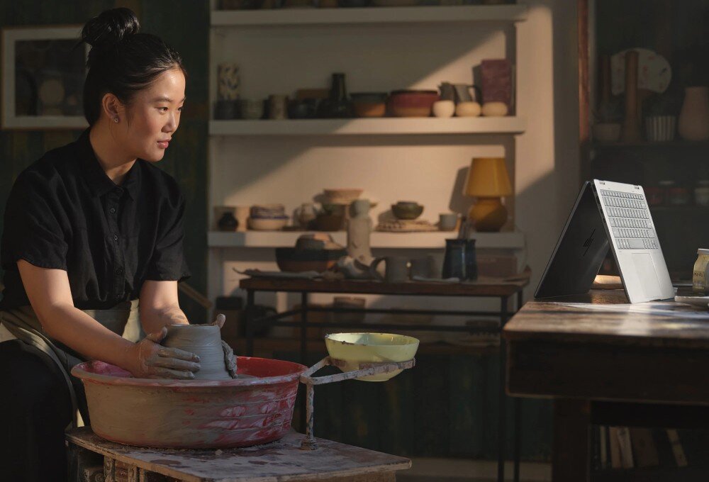 Laptop HP Envy x360 14-FA0014NW Kobieta w ciemnym ubraniu lepi naczynie z gliny na kole garncarskim, przed nią ustawiony laptop w pozycji odwróconej litery „V”, bateria, czas działania, ładowanie