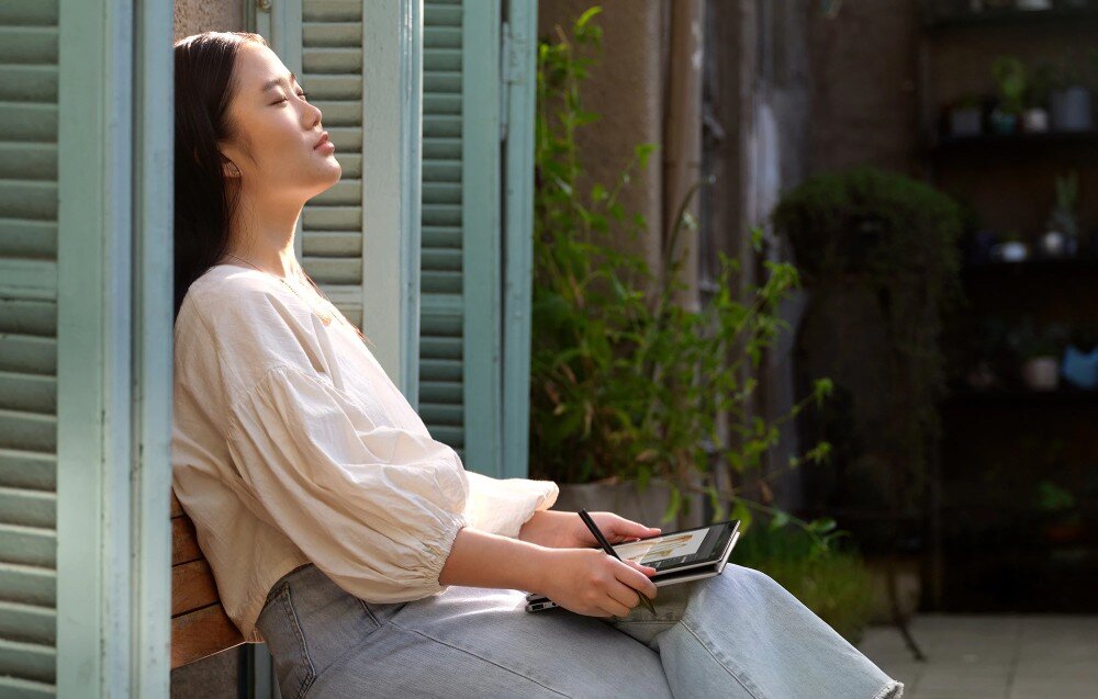 Laptop HP Envy x360 14-FA0014NW Kobieta siedzi na zewnątrz, odpoczywając na ławce, z zamkniętymi oczami, trzymając laptop w trybie tabletu i rysik w dłoni, zabezpieczenia, szyfrowanie TPM, zaślepka obiektywu