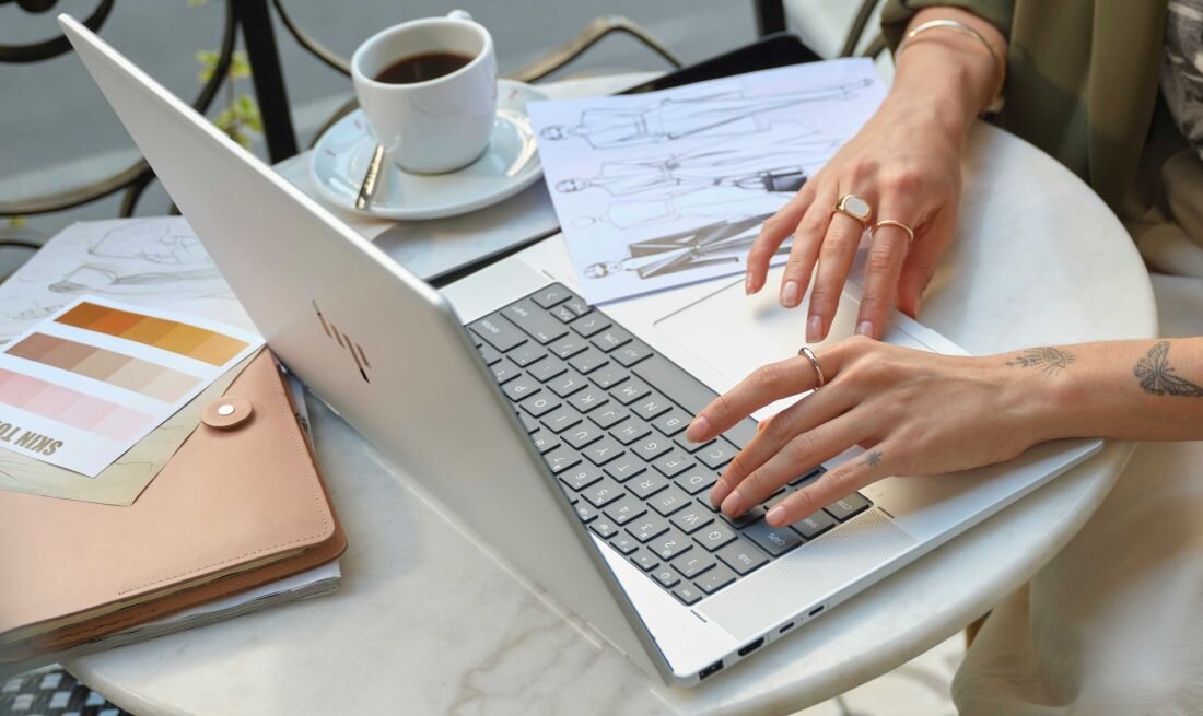 Laptop HP Envy x360 - Kobieta pracująca przy stole z laptopem HP Envy x360, otoczona przyjemną atmosferą.
