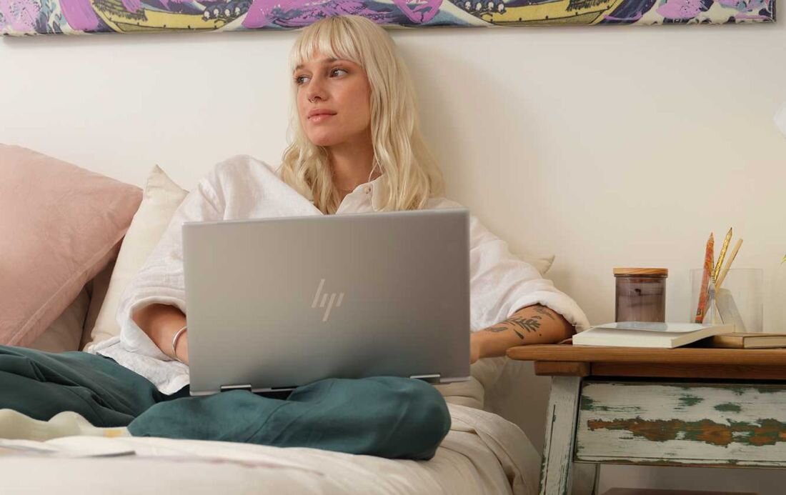Kobieta siedzi na łóżku, korzystając z laptopa HP Envy x360. Pamięć wewnętrzna LPDDR5-SDRAM