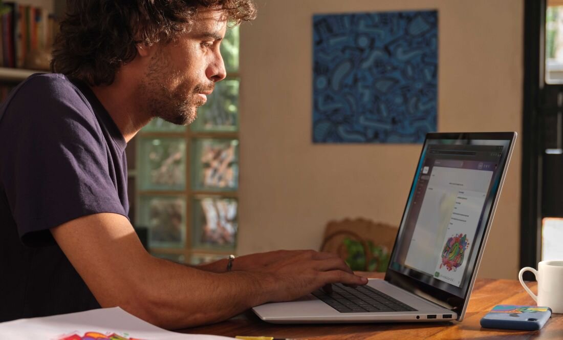 Mężczyzna siedzi przy stole z laptopem HP Envy x360, skupiony na pracy.   