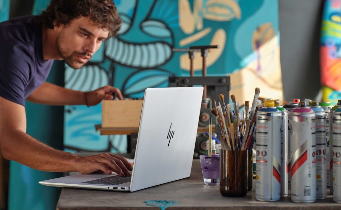 Mężczyzna korzystający z laptopa HP Envy x360 przed żywym muralem. Wi-Fi 7 (802.11be) Bluetooth 5.4 