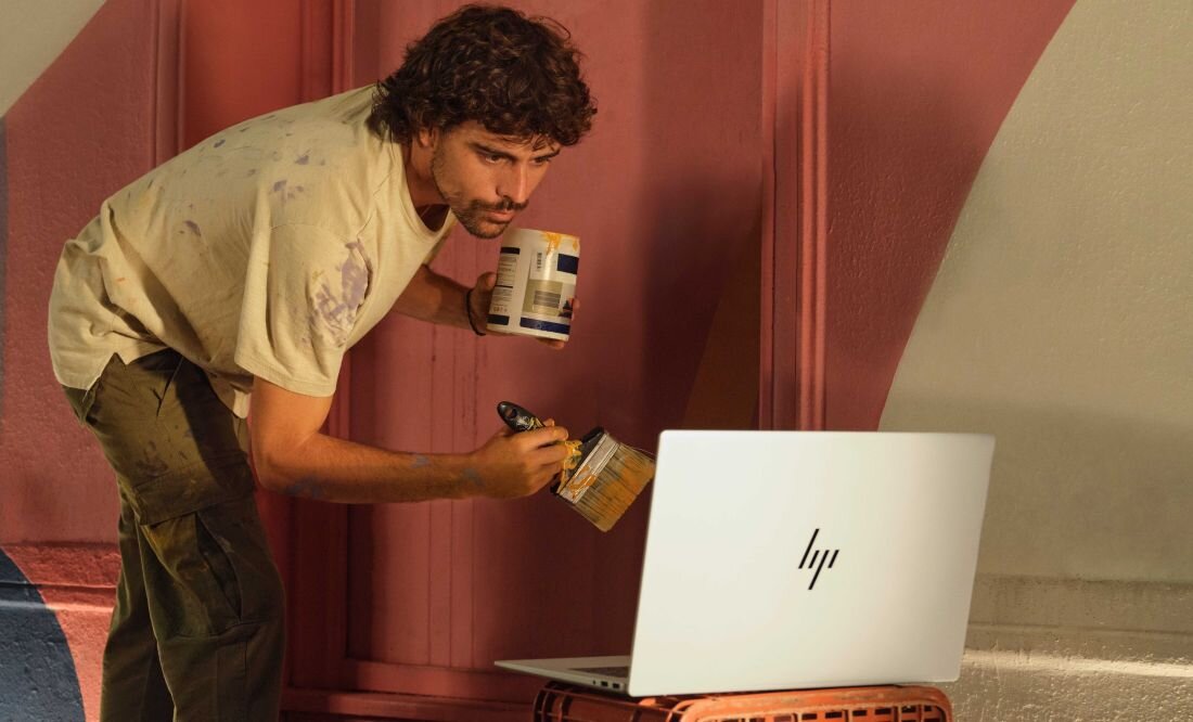 Mężczyzna używa pędzla do malowania, koncentrując się na pracy przy laptopie HP Envy x360. aluminium z recyklingu Certyfikat EPEAT Gold z Climate+ 