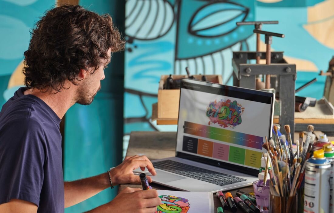 Mężczyzna z laptopem HP Envy x360 pracuje w tle kolorowego muralu. Dysk SSD PCIe NVMe 4.0 