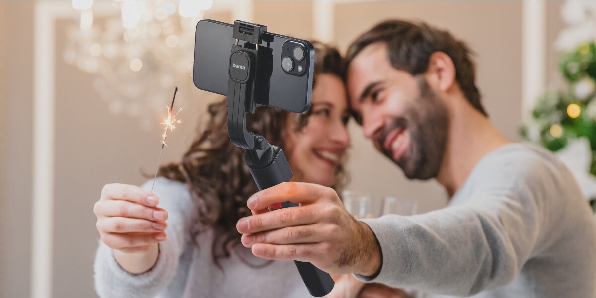 Uchwyt selfie HAMA Fancy Stand 70 II Pełna swoboda ujęć uśmiechnieta para ze sztucznymi ogniami jedna z osób robi zdjecie smartfonem na sticku