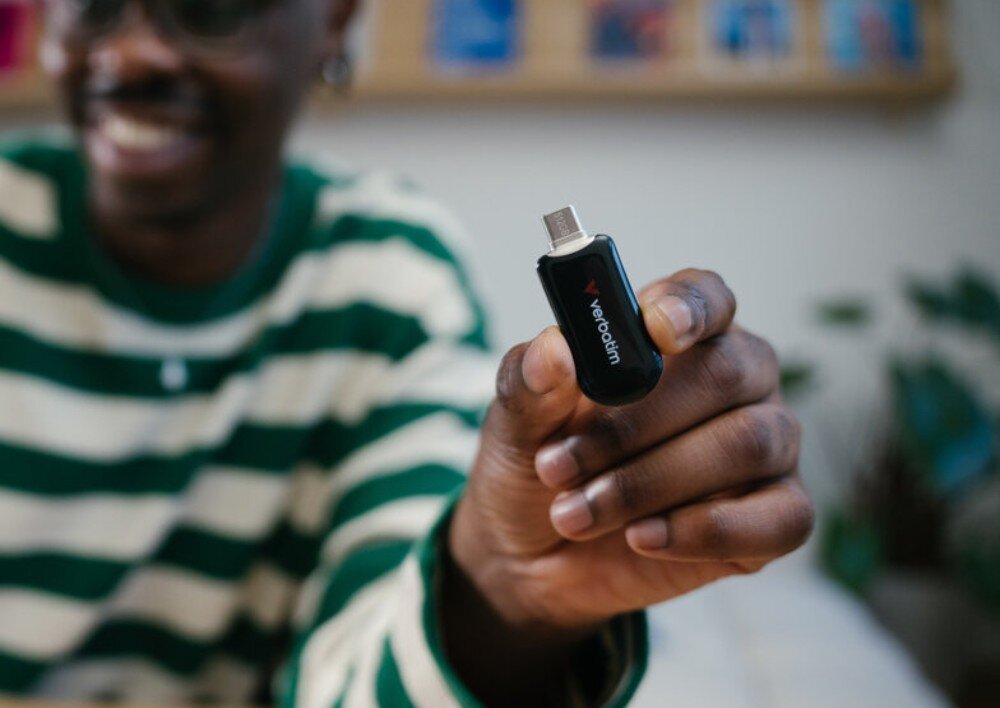 Pendrive VERBATIM Plectra Osoba w pasiaste koszulce trzyma przed sobą czarny pendrive z niebieskim akcentem i widocznym portem USB-C