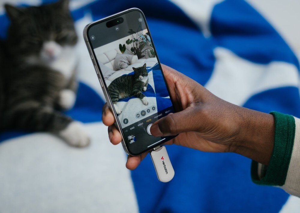 Pendrive VERBATIM Plectra Osoba leżąca na kanapie w okularach trzyma smartfon w jednej ręce oraz czarny pendrive w drugiej ręce