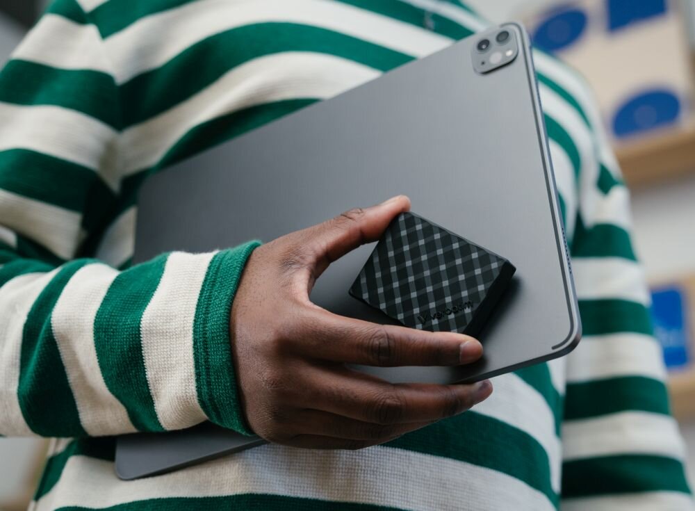Dysk VERBATIM Store 'n' Go Mini Diamond Osoba w zielono białym swetrze trzymająca pod pachą tablet i w dłoni mały czarny dysk przenośny w kratkę, opis