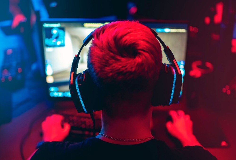 Procesor INTEL Core Ultra 9-285 Widok od tyłu na gracza w słuchawkach siedzącego przed monitorem podczas rozgrywki komputerowej w oświetleniu czerwono-niebieskim, układ graficzny, rozdzielczość, wydajność