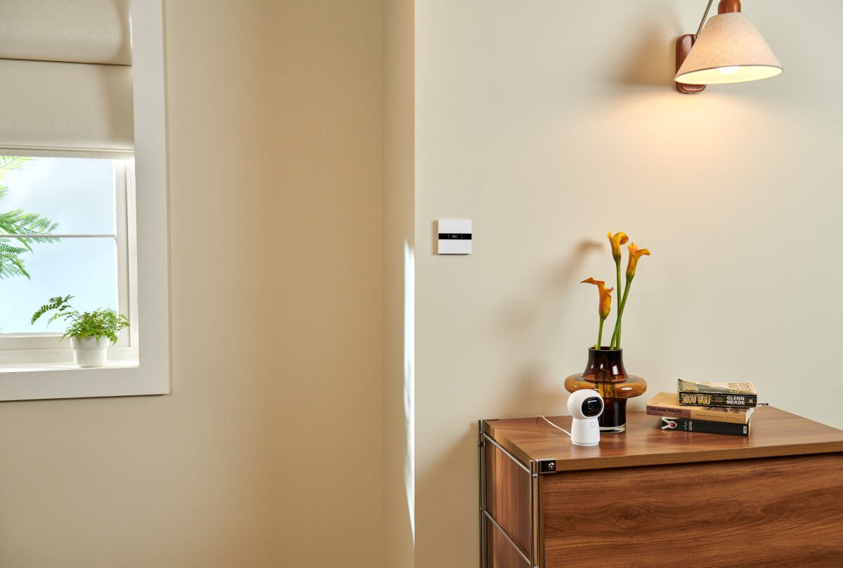 Przełącznik ścienny AQARA Display Switch V1 WS-K02D Zigbee/Bluetooth, Przełącznik w pokoju dziennym, zamontowany do ściany, w tle komoda, lampa, doniczka z kwiatem