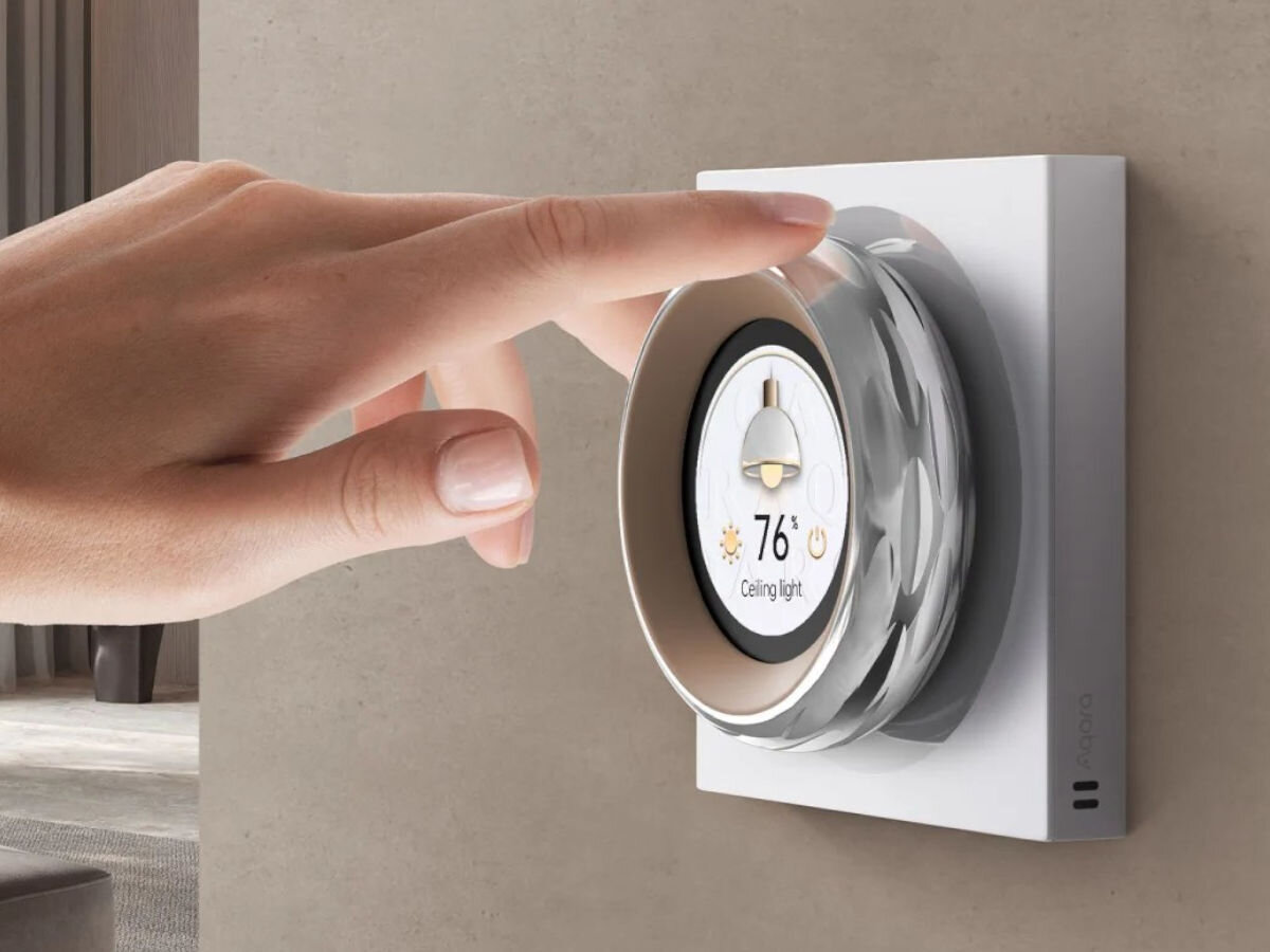Inteligentny sterownik AQARA Touchscreen Dial V1 EU DS-K01D, regulacja, obrót, ekran dotykowy, przełączniki, barwa światła, Ręka obsługuje regulacje sterownika przymocowanego do ściany, w tle pokój