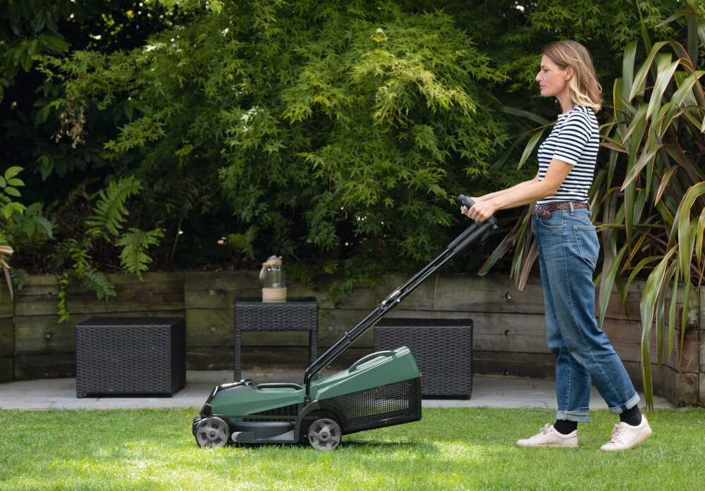 Kosiarka akumulatorowa BOSCH CityMower 18V-32-300 06008B9A0A ogród trawnik kobieta kosi trawę w ogrodzie w tle meble ogrodowe stalowy nóż obrotowy o szerokości 32 cm redukuje liczbę przejść podczas pracy równomierne i czyste cięcie