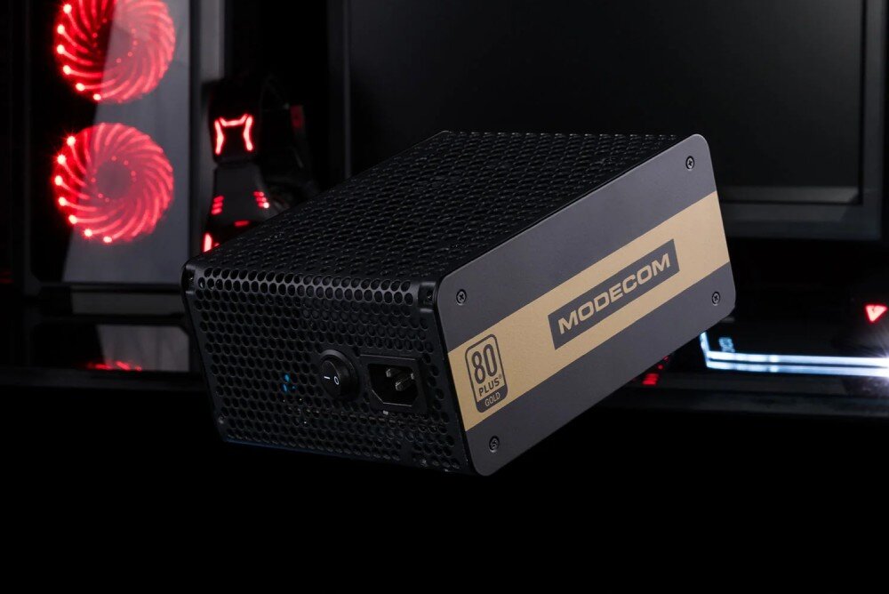 Komputer MAD DOG COUGAR-UNIFACE-I02WR32WP Czarny zasilacz MODECOM z certyfikatem 80 Plus Gold, umieszczony na tle gamingowego stanowiska z podświetleniem RGB