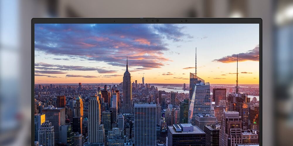 Ekran laptopa ASUS Zenbook 14 z widokiem na panoramę miasta podczas zachodu słońca, cienkie ramki, funkcja automatycznej regulacji jasności.