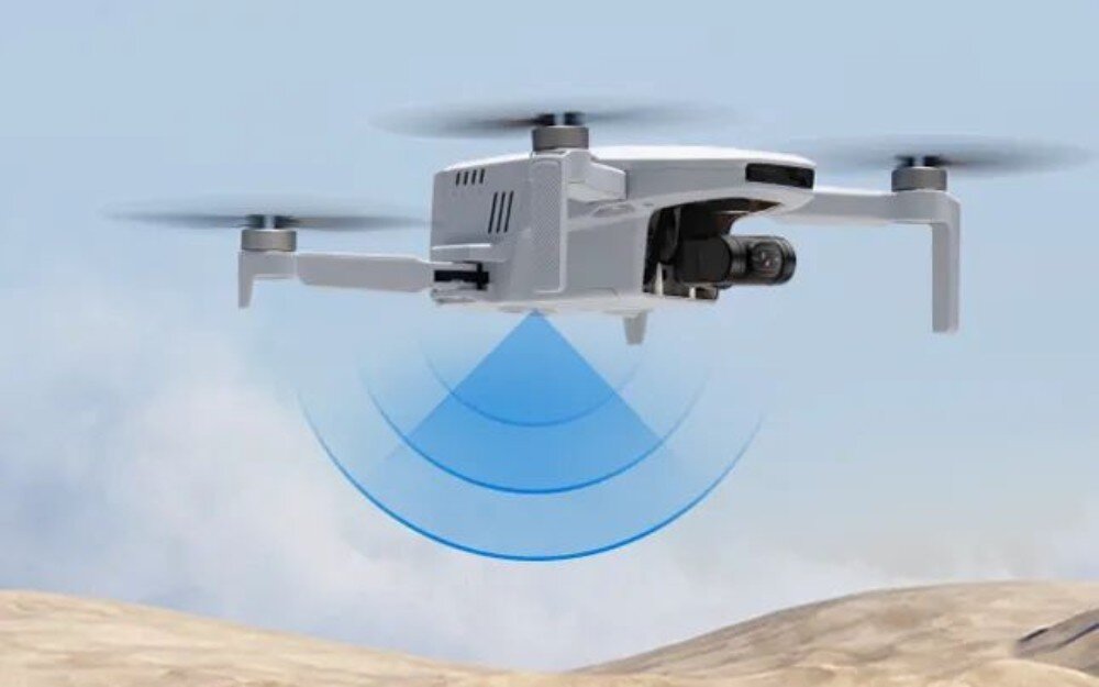 Dron POTENSIC Atom Body Dron wiszący nad piaszczystym terenem z grafiką niebieskich fal symbolizującą działanie czujników