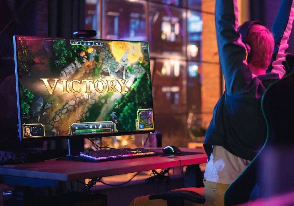 Dysk MSI Spatium M560 Osoba siedząca przed monitorem z wyświetlonym napisem 'Victory' w grze komputerowej, unosi ręce w geście radości, czas reakcji, wydajność, odczyt losowy