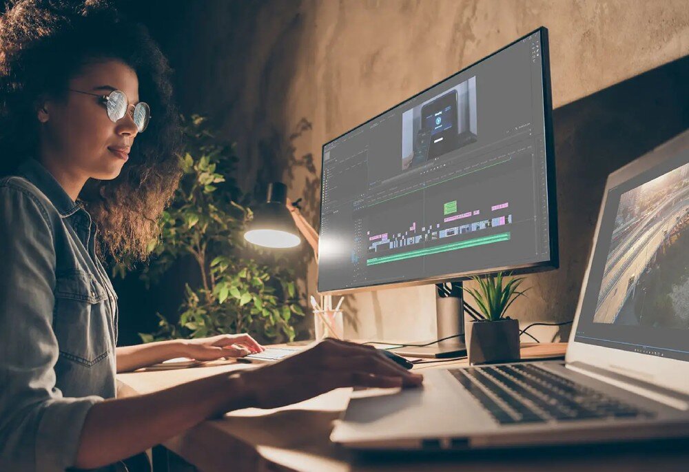 Dysk MSI Spatium M560 Kobieta pracująca przy biurku z laptopem i dużym monitorem, na ekranie widoczny interfejs do edycji wideo, dostęp do plików, czas oczekiwania