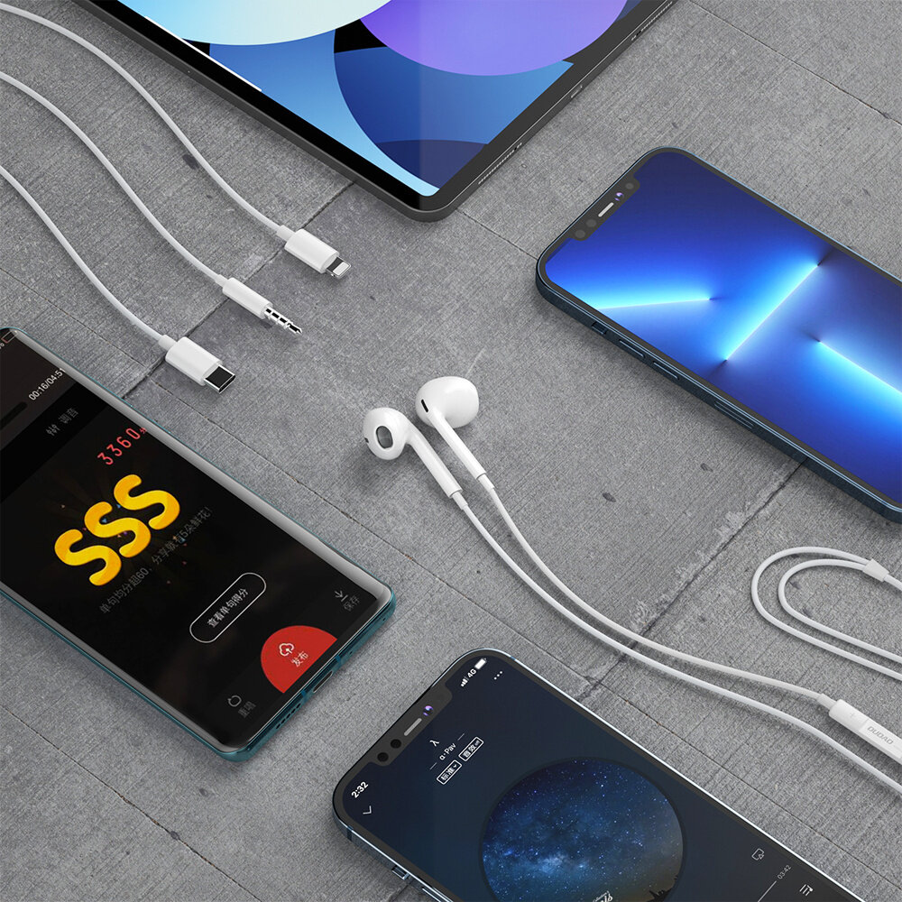 Na szarej powierzchni leżą białe słuchawki douszne z kablem zakończonym złączem minijack 3.5 mm. Obok znajdują się różne urządzenia elektroniczne, w tym smartfony i tablet z widocznymi ekranami.