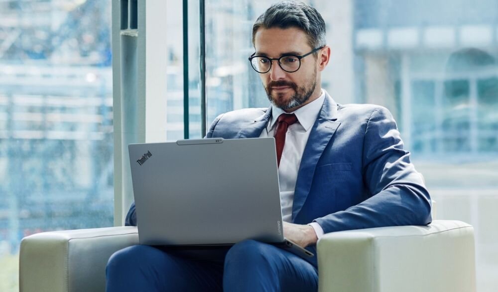 Biznesmen pracujący na laptopie Lenovo ThinkPad w biurze przy panoramicznym oknie - Wellness Mode 