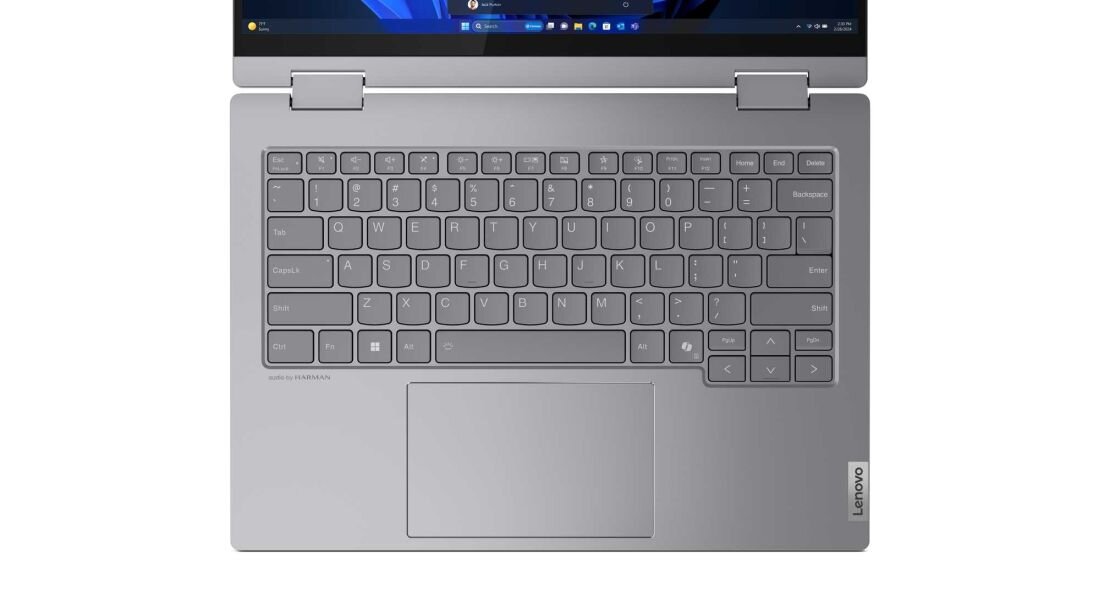 Widok z góry na laptop Lenovo ThinkBook 14 2-in-1 w srebrnej obudowie z pełnowymiarową klawiaturą, dużym touchpadem i zaawansowanymi zawiasami 360°, na niebieskim tle z interfejsem Windows 11 na ekranie. - Wygodna klawiatura
