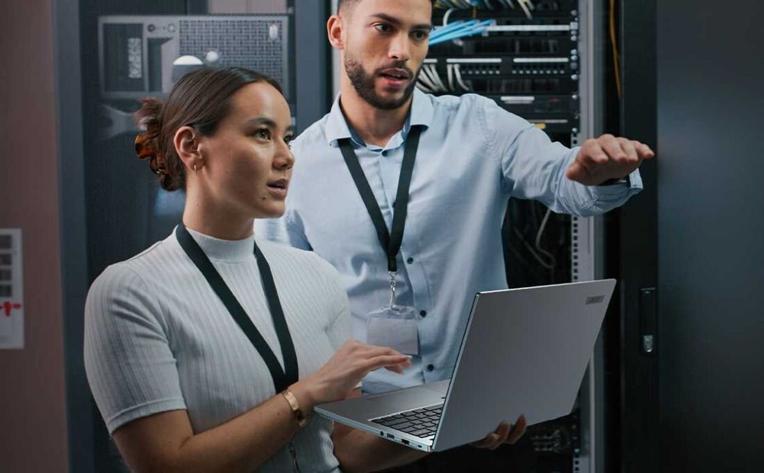 Dwie osoby stoją przed serwerem, trzymając laptopa ACER TravelMate P2.  - ACER PurifiedView i ACER PurifiedVoice 