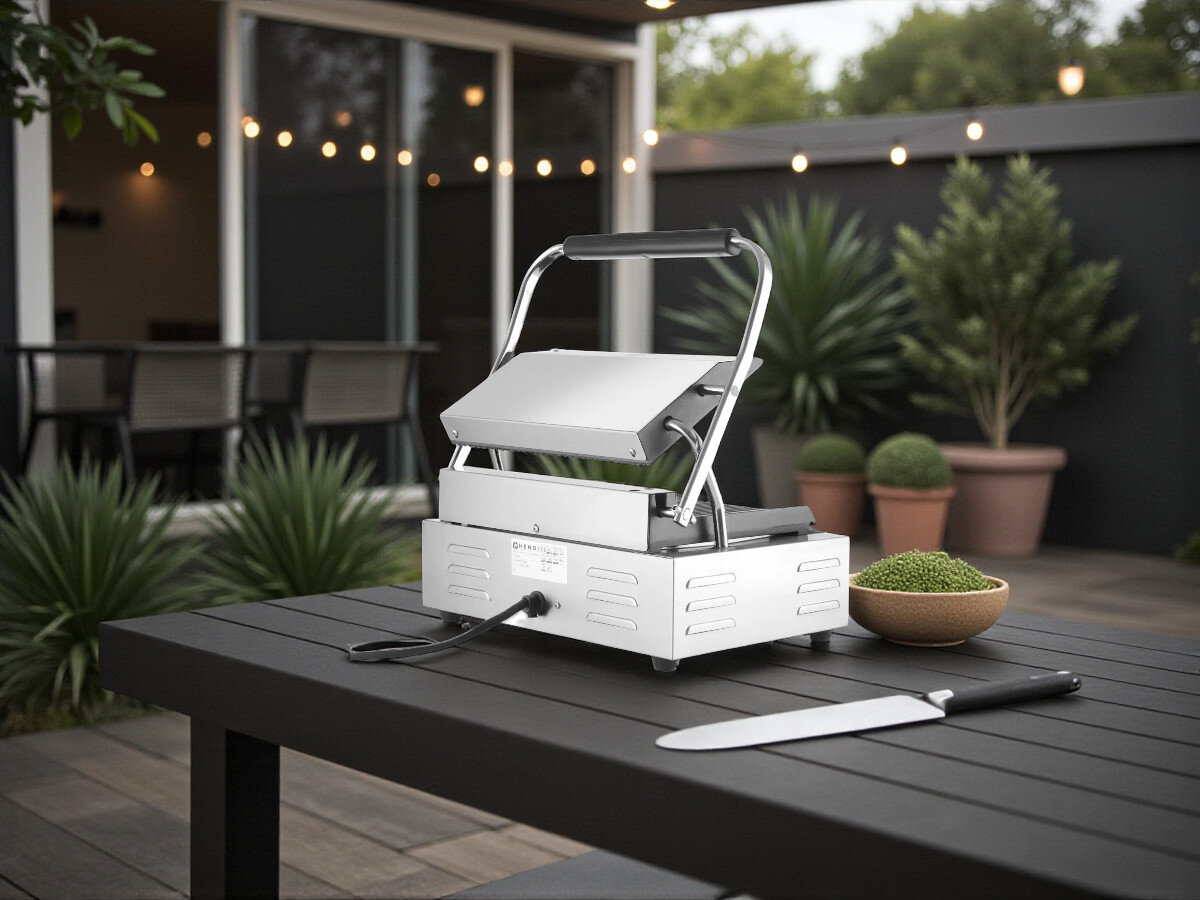 Grill elektryczny HENDI Panini 263655, wydajny grill, płynna regulacja, wskaźniki świetlne, wygodna obsługa, Grill kontaktowy Hendi Panini 263655 na stole ogrodowym, widok z tyłu na podłączony kabel oraz otoczenie z zielonymi roślinami, zachód słońca.