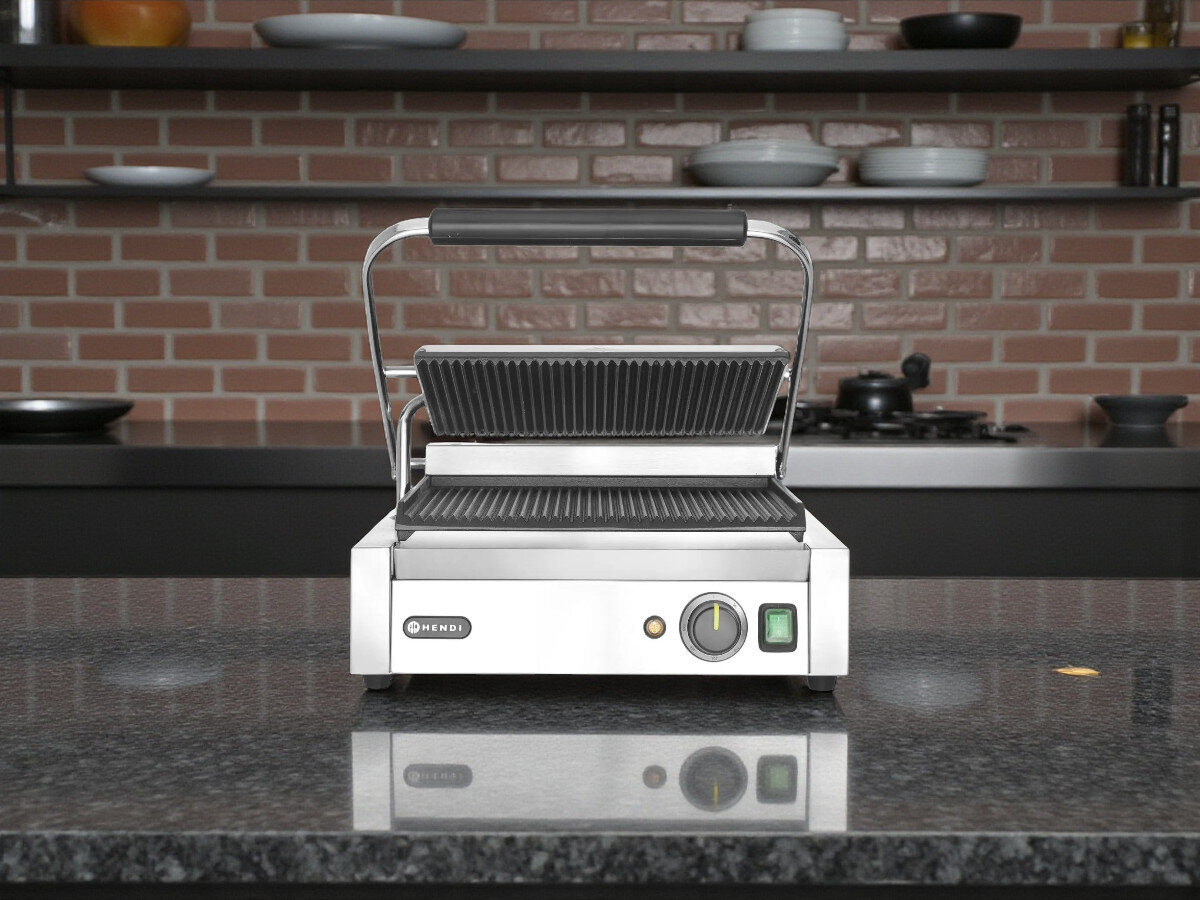 Grill elektryczny HENDI Panini 263655, stal, ciężar, stabilność, trwałość, Hendi Panini 263655 na stalowym blacie w kuchni restauracyjnej na tle ceglanej ściany, uchylona pokrywa pokazuje powierzchnie grillujące.