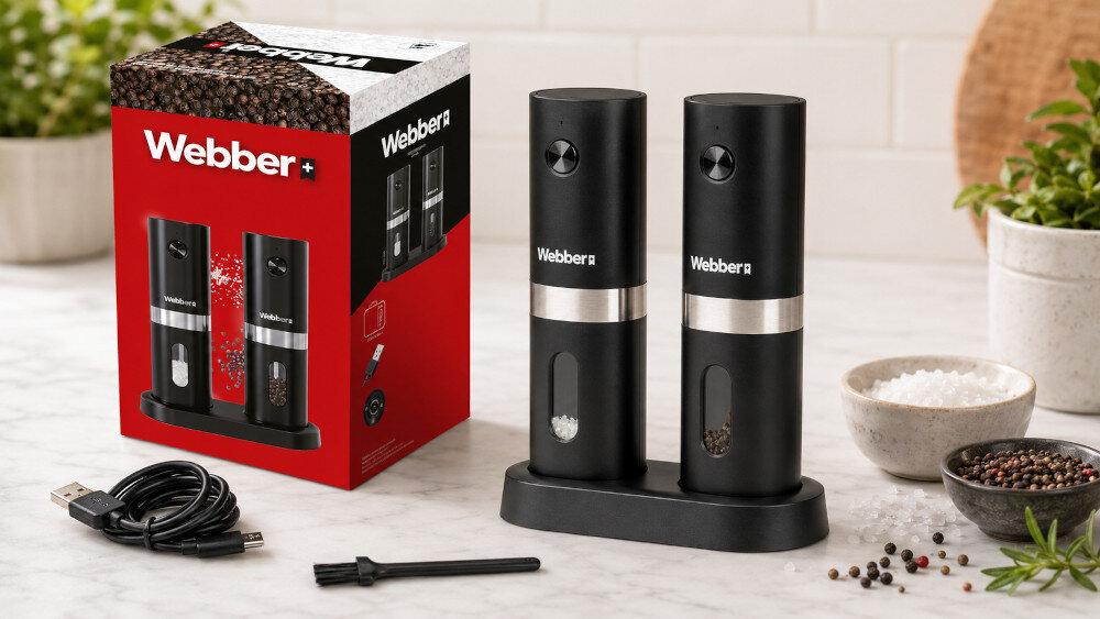 Na obrazie widoczny jest zestaw dwóch czarnych młynków do przypraw marki Webber, umieszczonych na podstawce, obok opakowania z logo Webber. W tle znajdują się miseczki z solą i pieprzem oraz kabel USB i mały pędzelek.