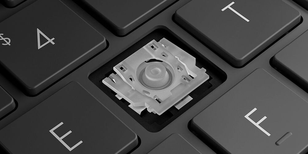 Zbliżenie na mechanizm klawisza laptopa ASUS Vivobook S 16 OLED z technologią ErgoSense – widoczny biały, plastikowy stabilizator klawisza z centralnym punktem nacisku, otoczony czarnymi klawiszami z białymi oznaczeniami, w tym klawisze z symbolami strzałek i literą F. - Klawiatura ErgoSense