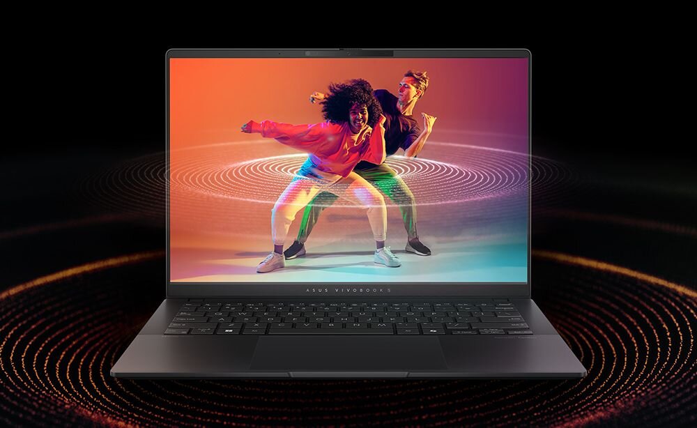 Laptop ASUS Vivobook S 16 OLED na czarnym tle z koncentrycznymi, pomarańczowymi okręgami wokół urządzenia, na ekranie dynamiczna scena dwóch tancerzy w kolorowych strojach na tle gradientu od pomarańczowego do fioletowego, pod ekranem napis ASUS VIVOBOOK, ilustracja zaawansowanego systemu dźwiękowego. - czysty dźwięk