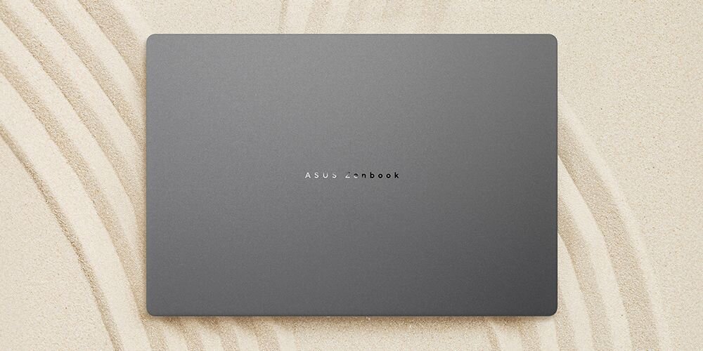 Zamknięty laptop ASUS Zenbook na beżowym tle z falującymi liniami piasku, demonstracja łatwości czyszczenia powierzchni dzięki specjalnej powłoce antyodciskowej PVD - Odporność na rozlane płyny