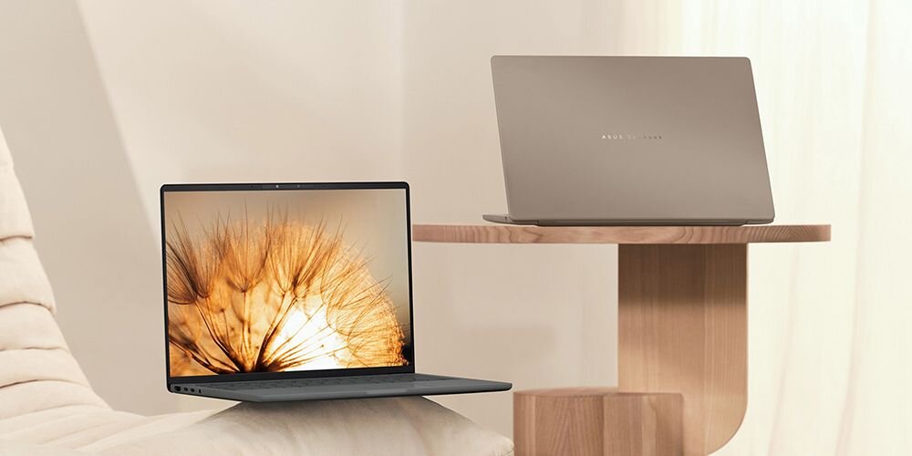 Dwa laptopy ASUS Zenbook na drewnianej półce - jeden w kolorze ciemnoszarym z otwartym ekranem wyświetlającym dmuchawiec, drugi w kolorze beżowym z zamkniętą klapą, dwie eleganckie opcje kolorystyczne - Iceland Gray Zabriskie Beige