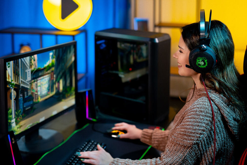 Komputer MAD DOG ENDORFY500AIR-I09WR32WH i5-14400F 32GB RAM 1TB SSD GeForce RTX4060 DLSS 3 Wi-Fi Windows 11 Home 
							graj płynnie w ulubione gry kobieta patrząca na monitor, klawiatura myszka, słuchawki, w tle komputer na biurku i logo sklepu