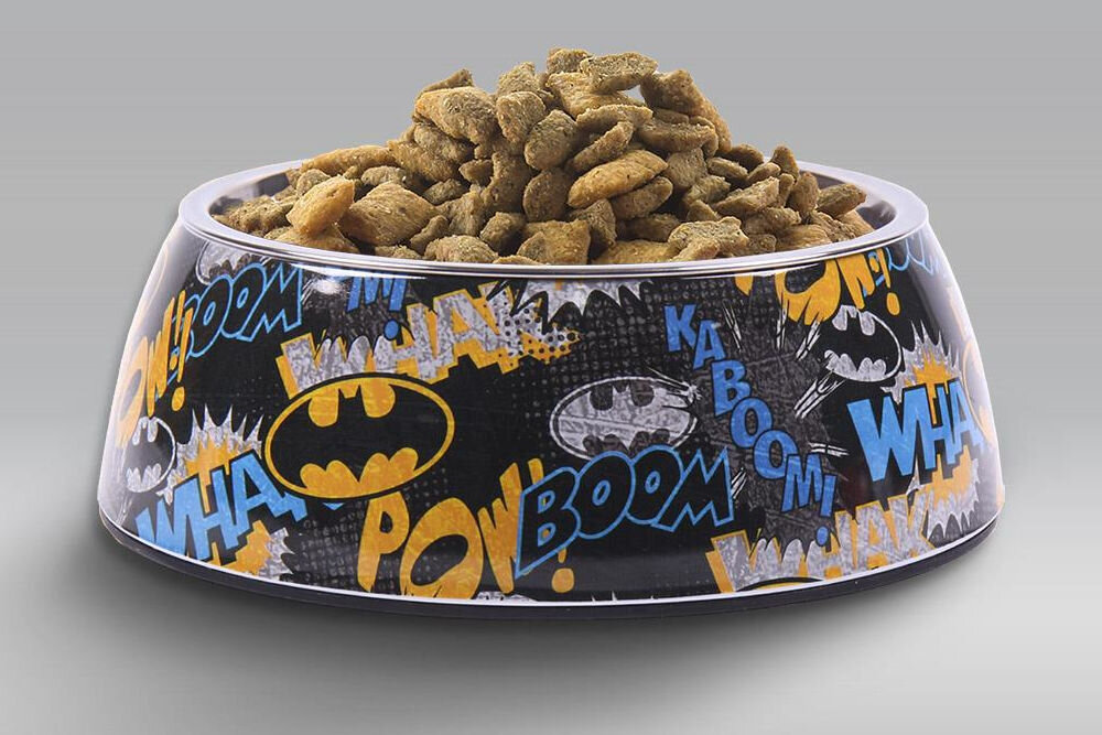 Miska dla psa CERDA Batman, licencjonowany design DC Comics, żywe kolory, modny wzór dla psa, wystrój wnętrza - Na zdjęciu znajduje się miska dla psa z motywem komiksowym, wypełniona suchą karmą. Na misce widoczne są napisy WHAM!, POW!, BOOM! oraz logo z symbolem nietoperza.