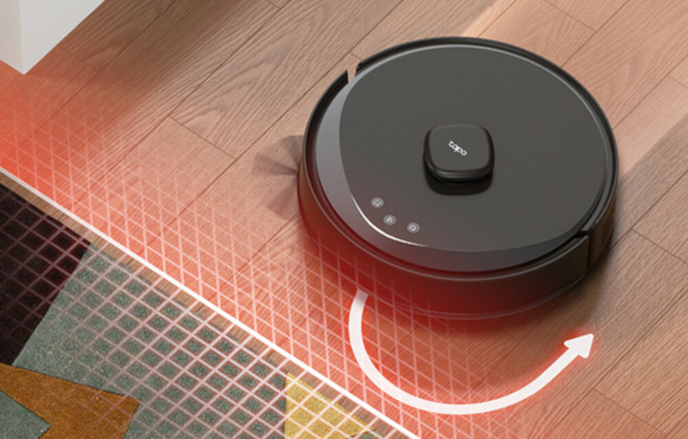Na drewnianej podłodze znajduje się okrągły robot sprzątający z logo \'tapo\' na górze. Widać czerwone linie i strzałkę wskazującą kierunek ruchu robota.